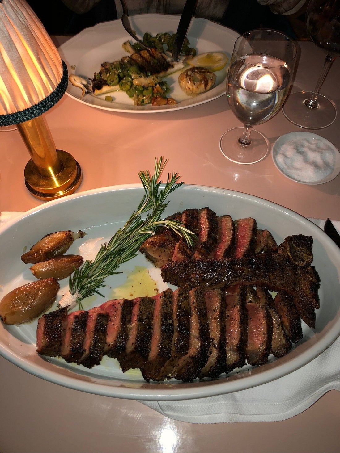 A sliced porterhouse steak garnished with a sprig of rosemary and served with roasted shallots on an oval platter.