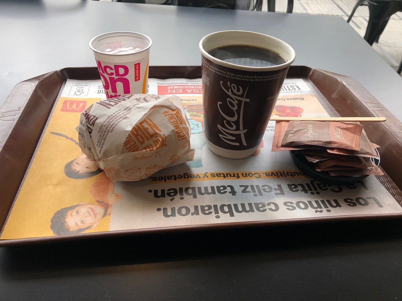 A tray containing a McDonald’s burger, a small drink, and a large McCafé coffee with packets of sugar.