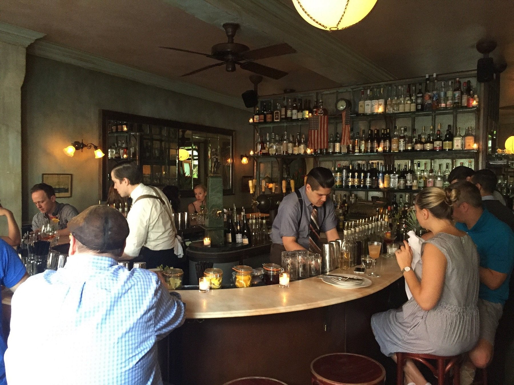 Patrons sit at curved bar seating while a bartender prepares drinks in front of a well-stocked liquor shelf.