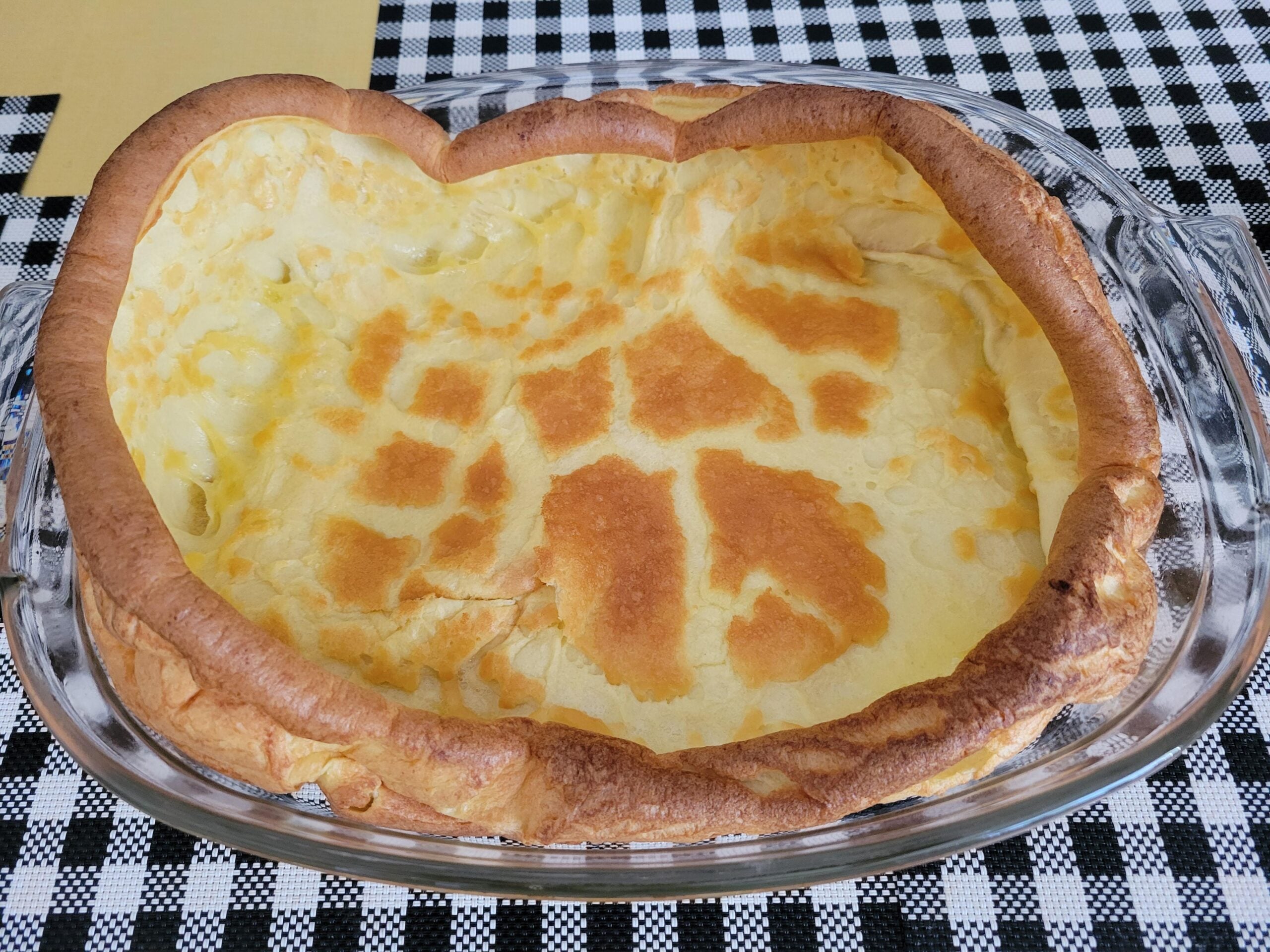 A golden-brown Dutch baby pancake in a glass baking dish sitting on a black and white checkered tablecloth.