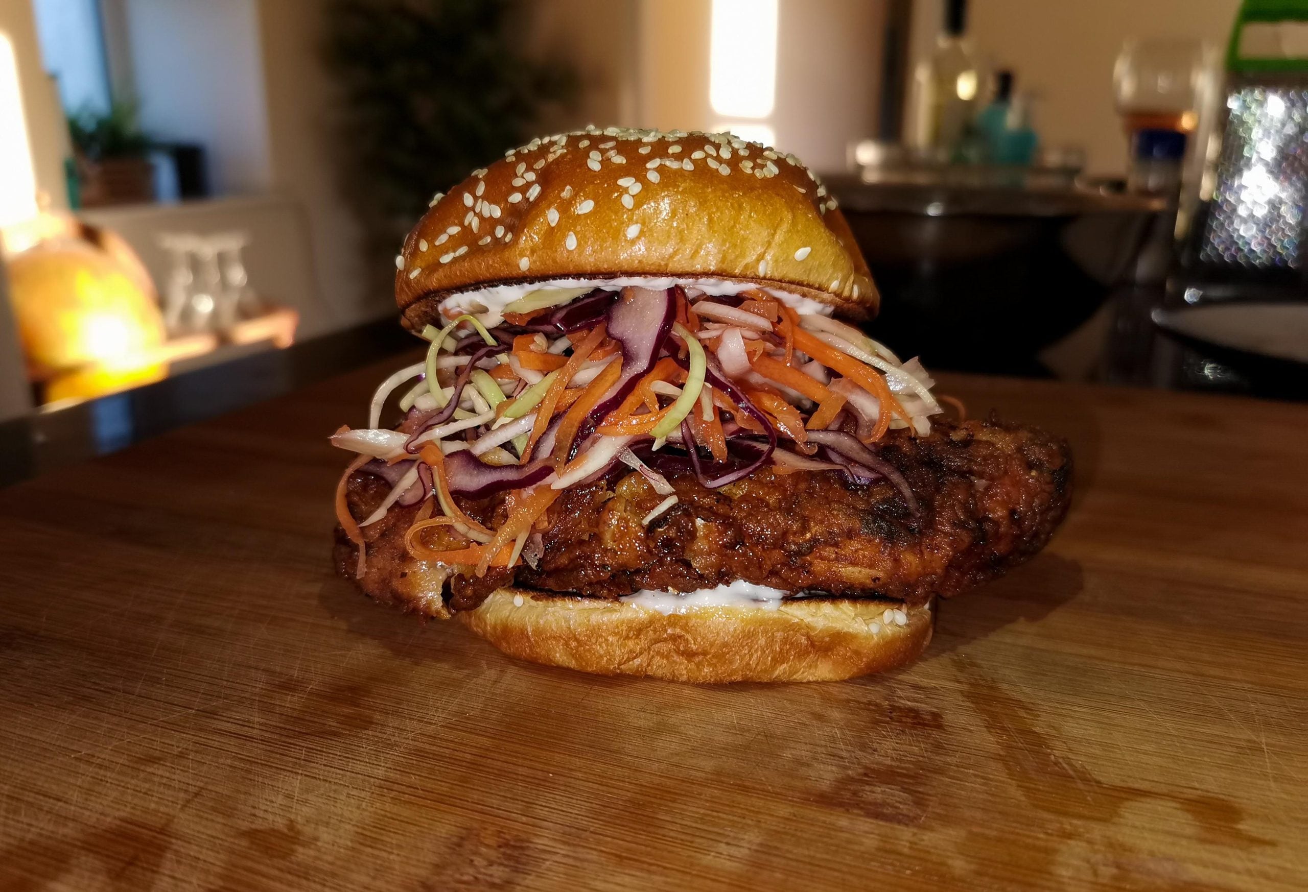 Fried chicken sandwich topped with red cabbage and carrot slaw on a sesame seed bun.