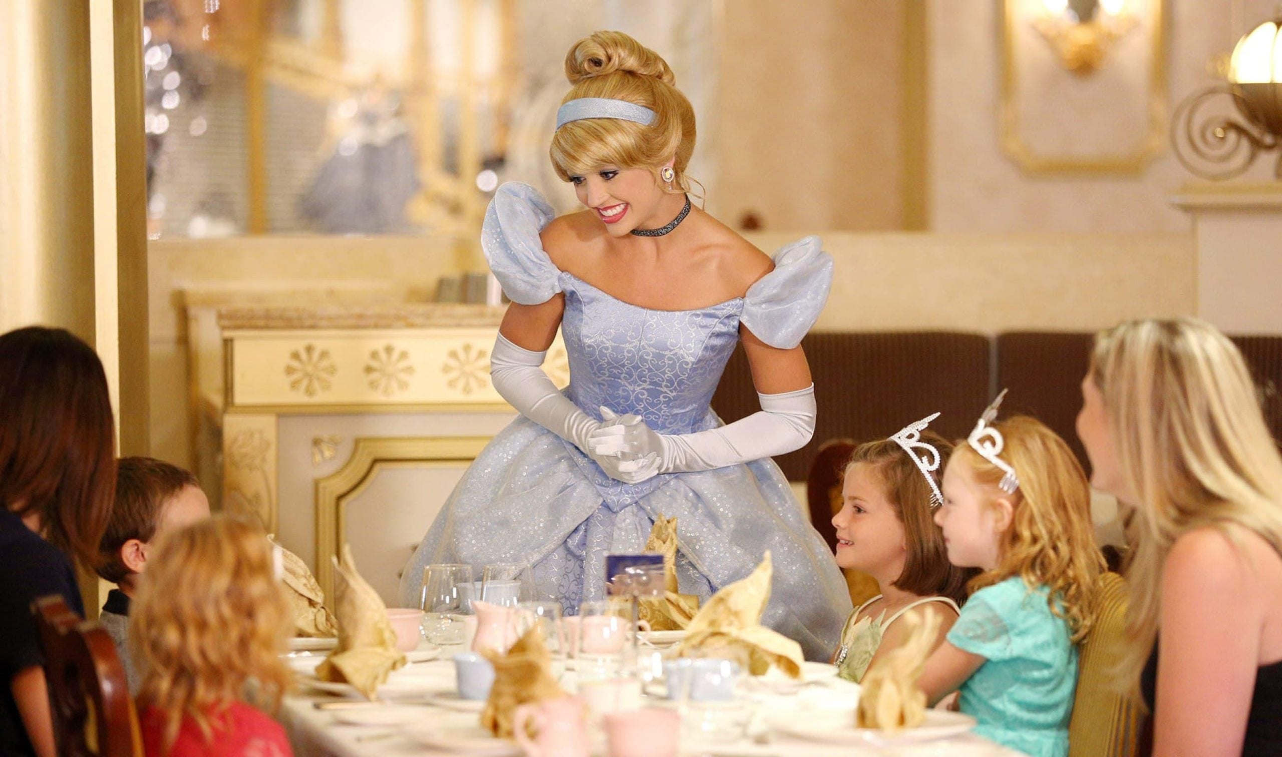 A performer dressed as Cinderella interacts with children at a table during a cruise ship character dining experience.