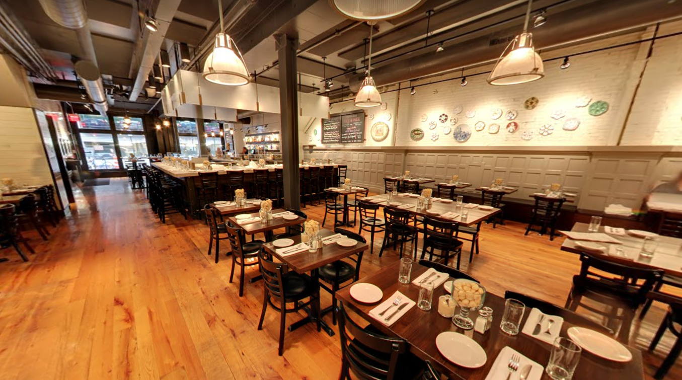 The interior of a restaurant with a long bar, wooden tables and chairs, and decorative plates displayed on the wall.