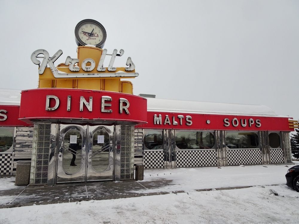 Kroll’s Diner with a vintage red and yellow exterior and a clock on the roof, surrounded by snow.