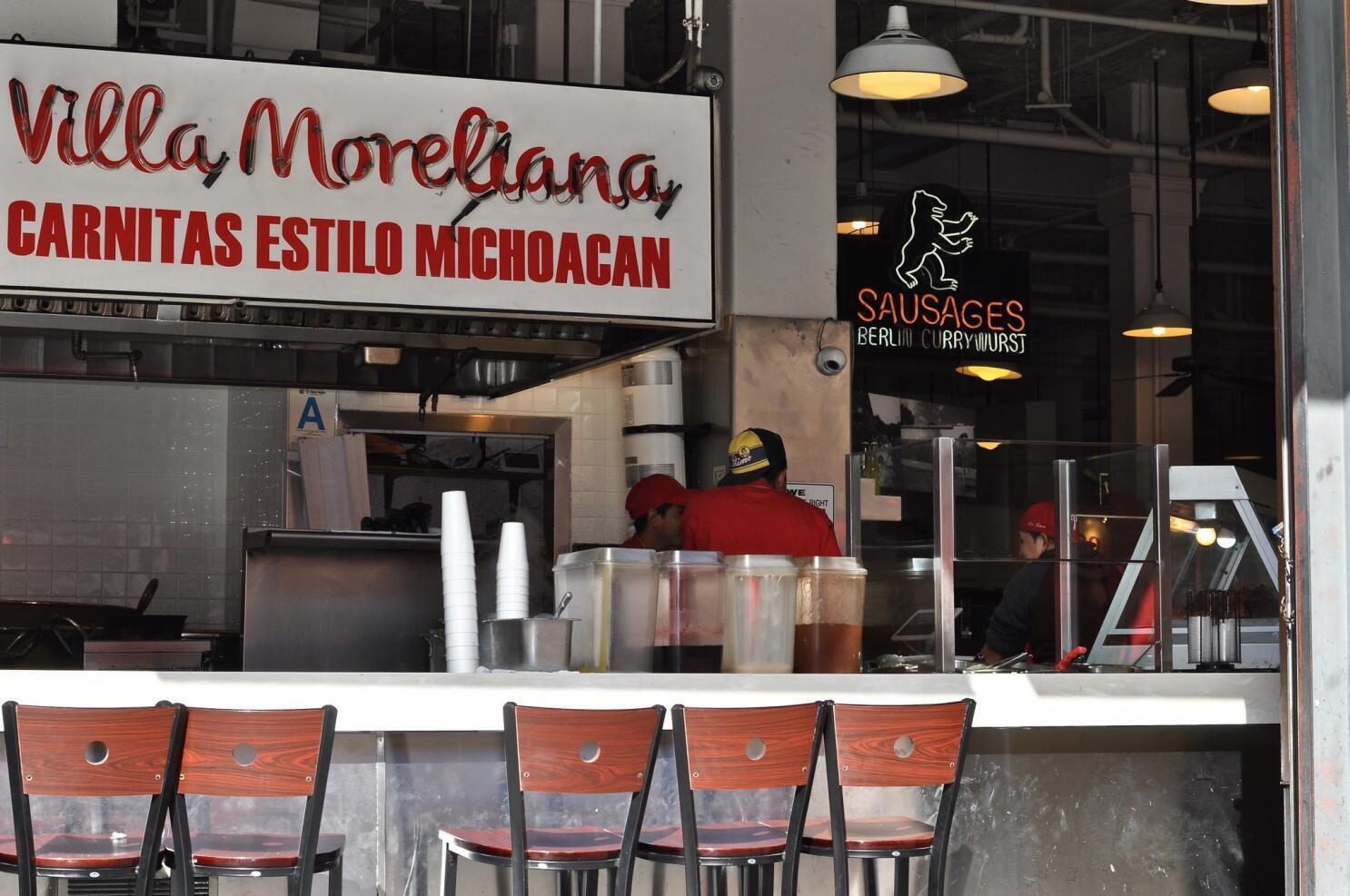 Villa Moreliana food stall with staff working behind a counter, and a sign for Berlin Currywurst sausages nearby.