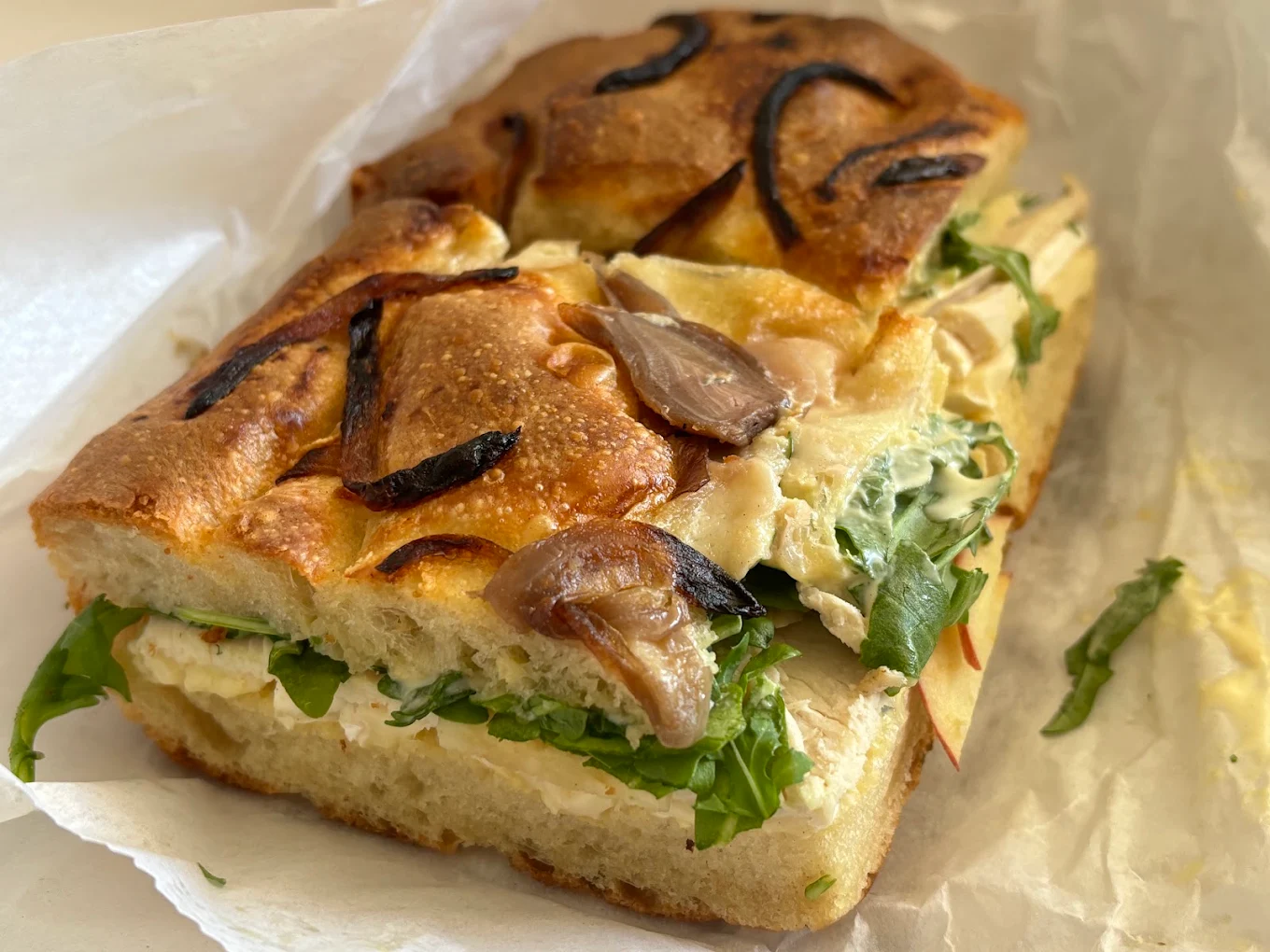 A focaccia sandwich topped with caramelized onions and filled with sliced meat, greens, and cheese.