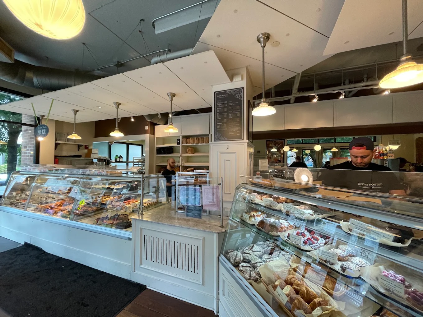 The interior of a bakery with two large glass display cases filled with pastries, and a staff member behind the counter.