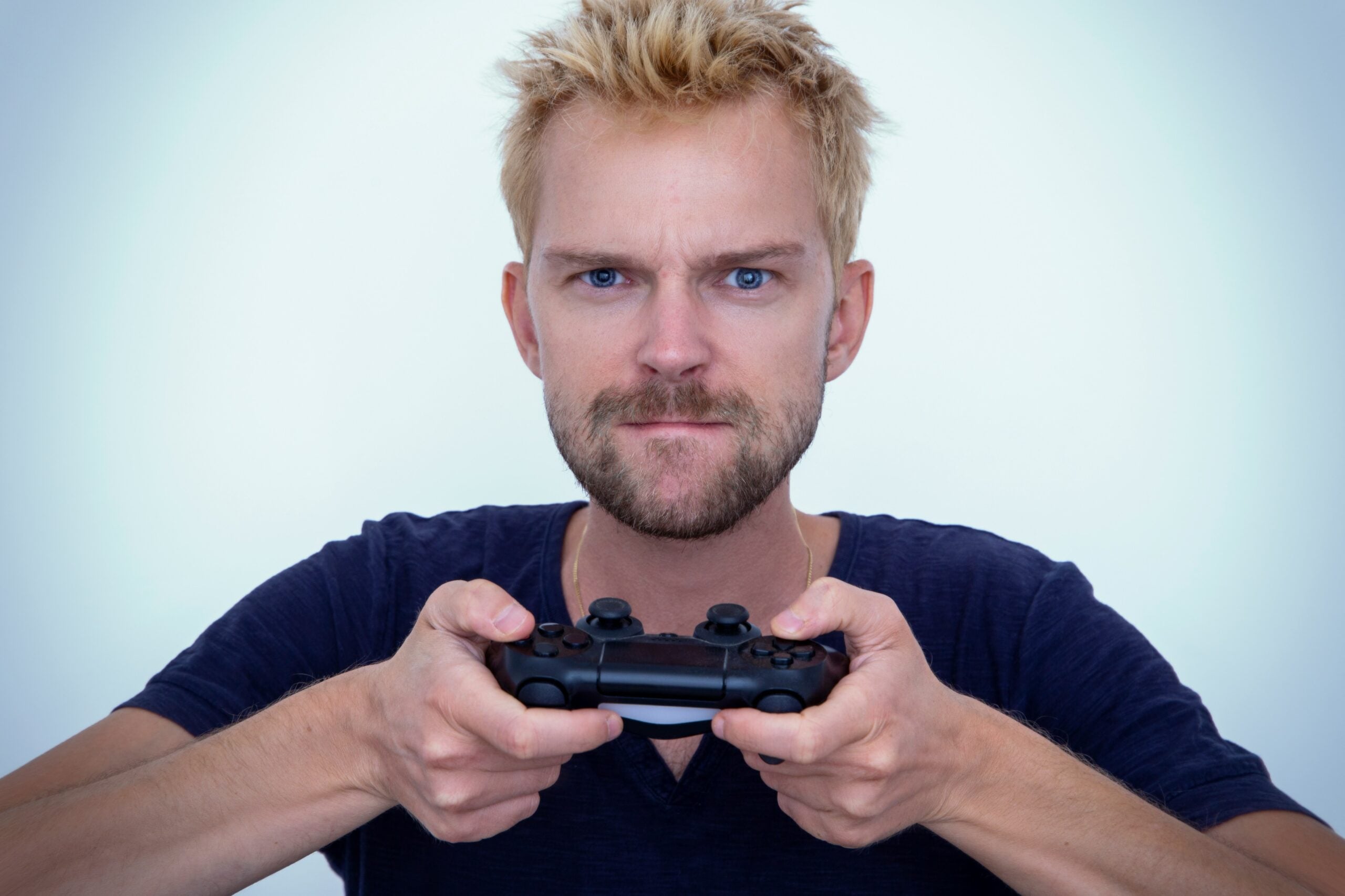 A man with a serious expression holding a black video game controller.