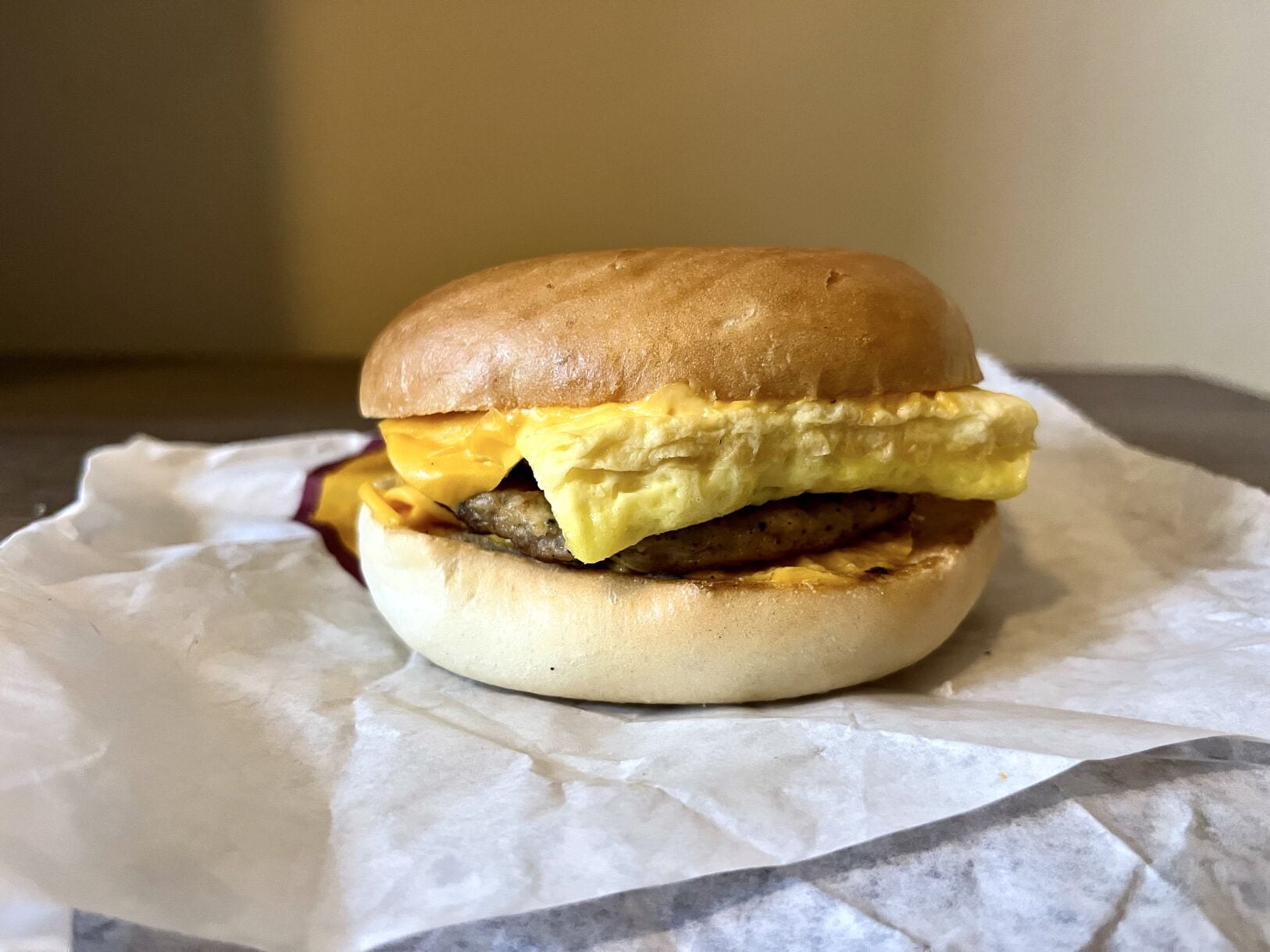 A breakfast sandwich with sausage, egg, and melted cheese on a bun, resting on a piece of paper.