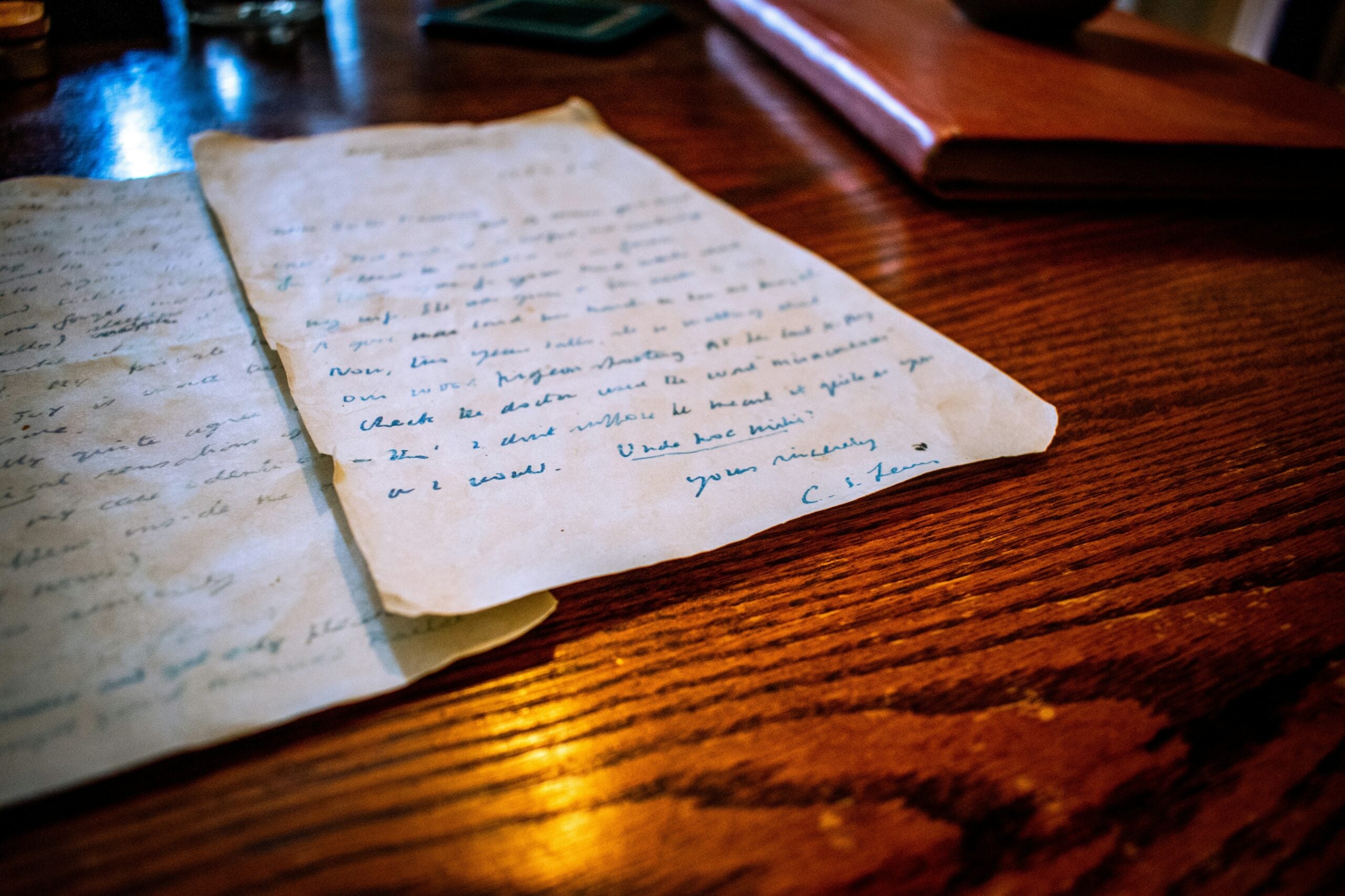 Handwritten letter on a wooden desk signed by C.S. Lewis as one of the paper records.
