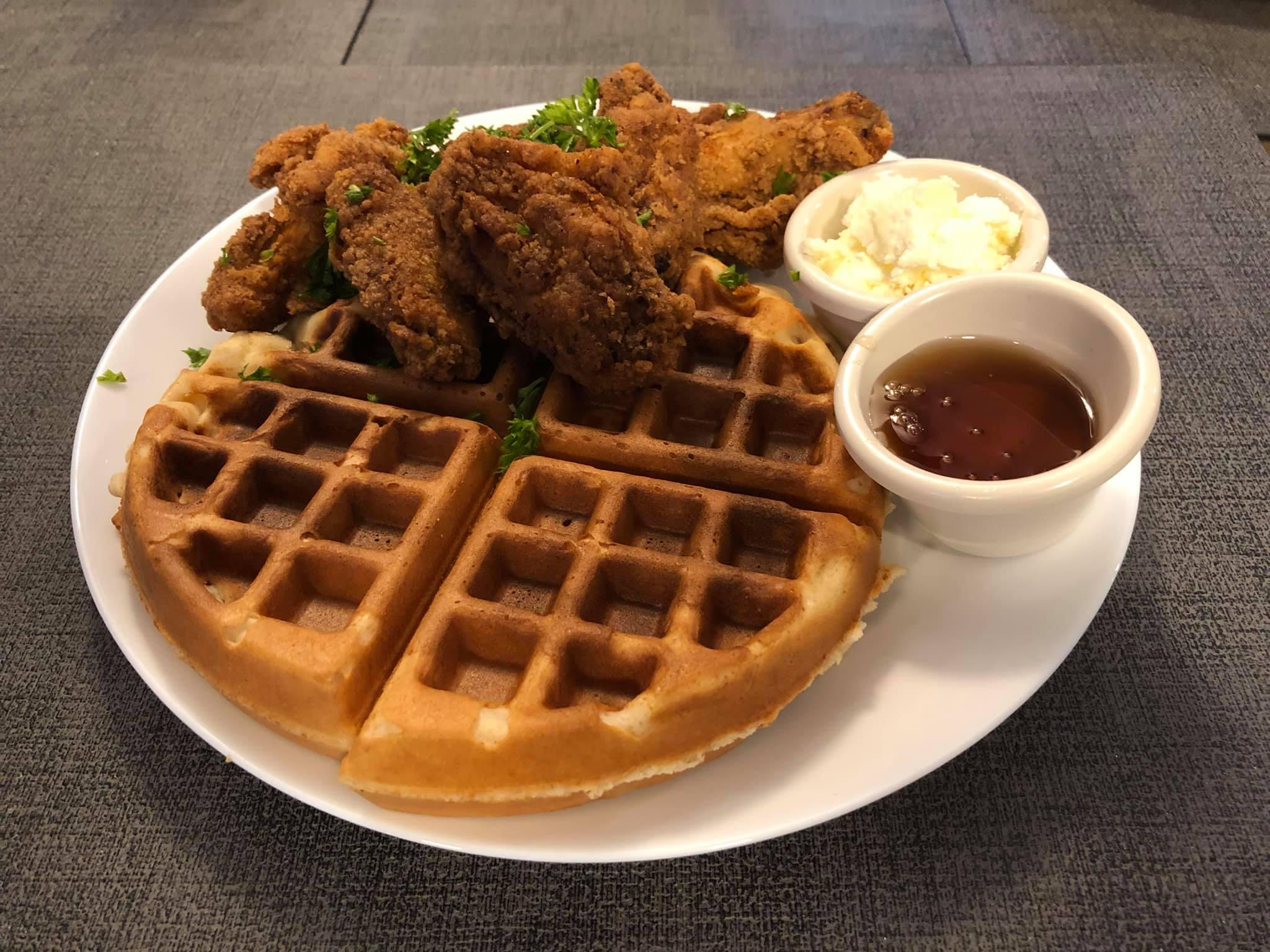 Fried chicken and a Belgian waffle on a white plate, served with small bowls of butter and syrup.