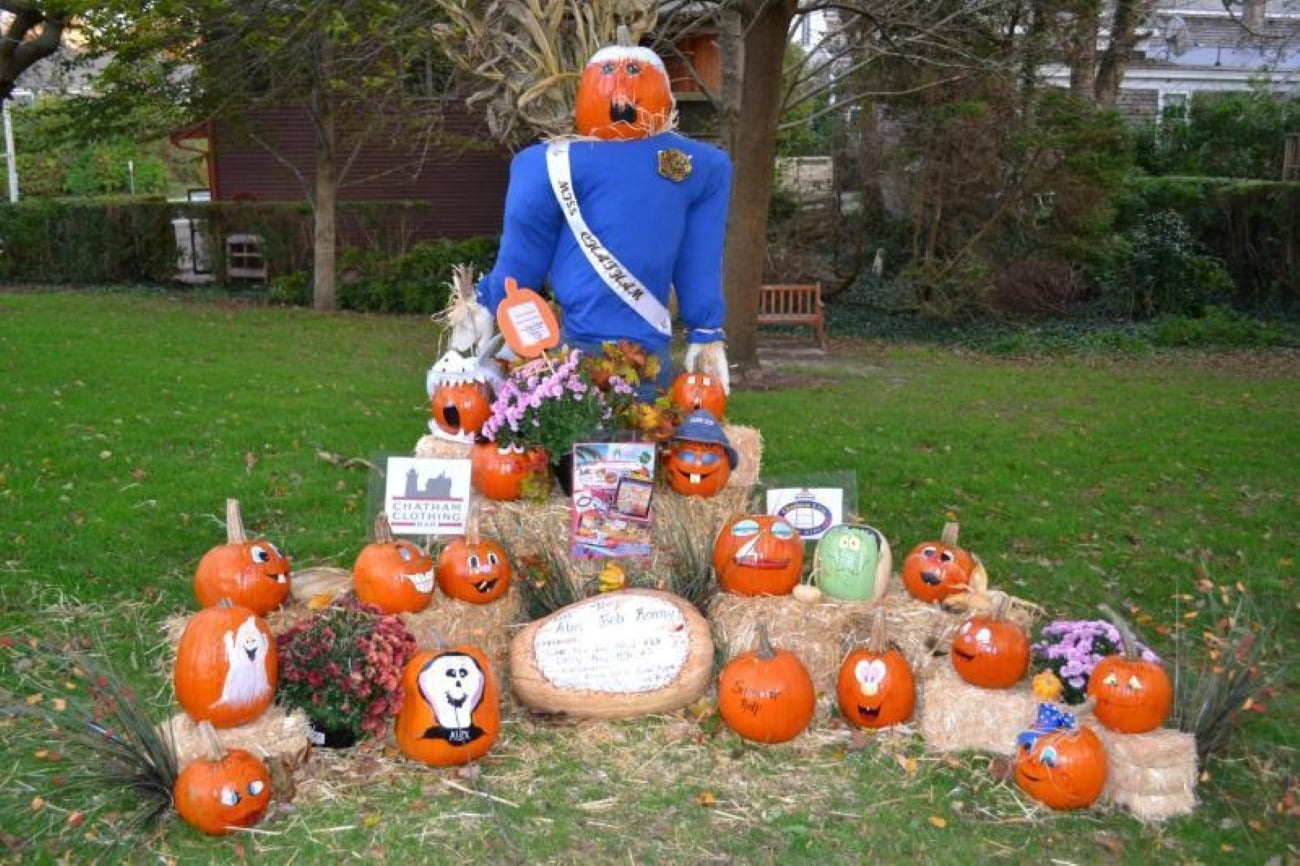 A large pumpkin-headed scarecrow wearing a “Miss Chatham” sash surrounded by many painted pumpkins and signs on hay bales.