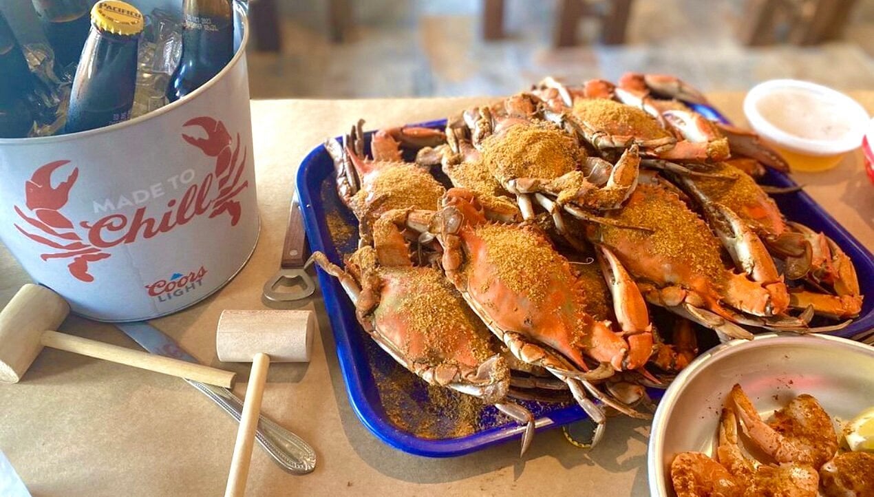 A large platter of steamed blue crabs seasoned with Old Bay, sitting next to a bucket of iced beer.