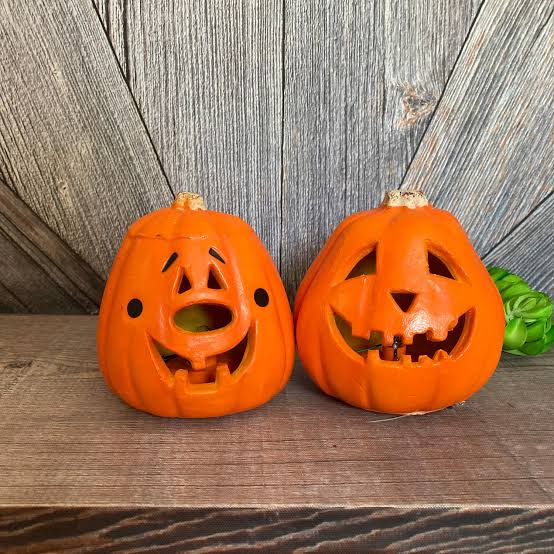 Two orange ceramic jack-o’-lanterns with carved faces sitting on a wooden surface.