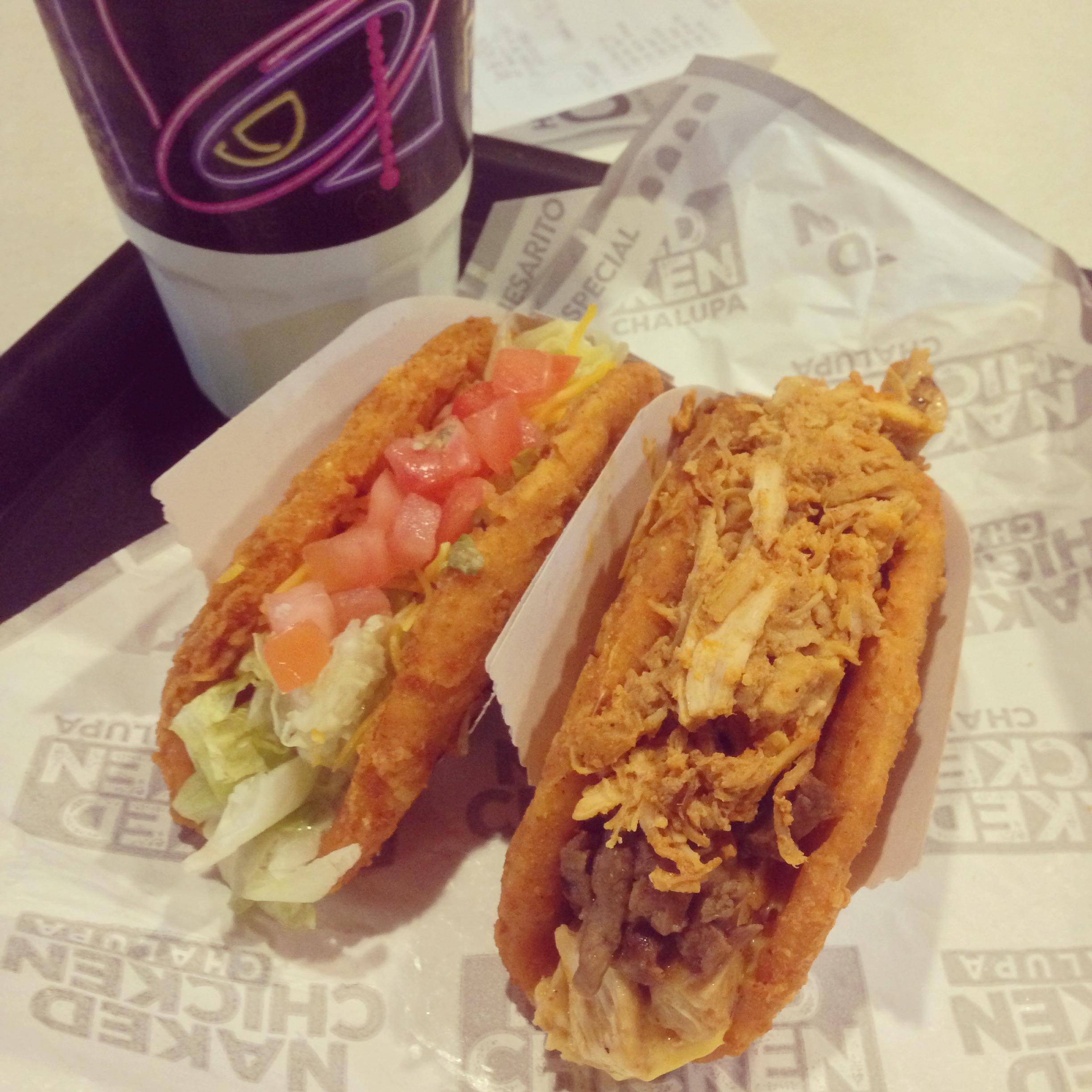 Two Naked Chicken Chalupas from Taco Bell, one topped with lettuce, tomatoes, and cheese, and the other with shredded chicken, sitting on a tray next to a drink cup.