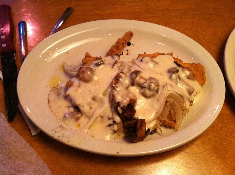 Breaded cutlet topped with mushroom gravy and sautéed onions on a white plate.