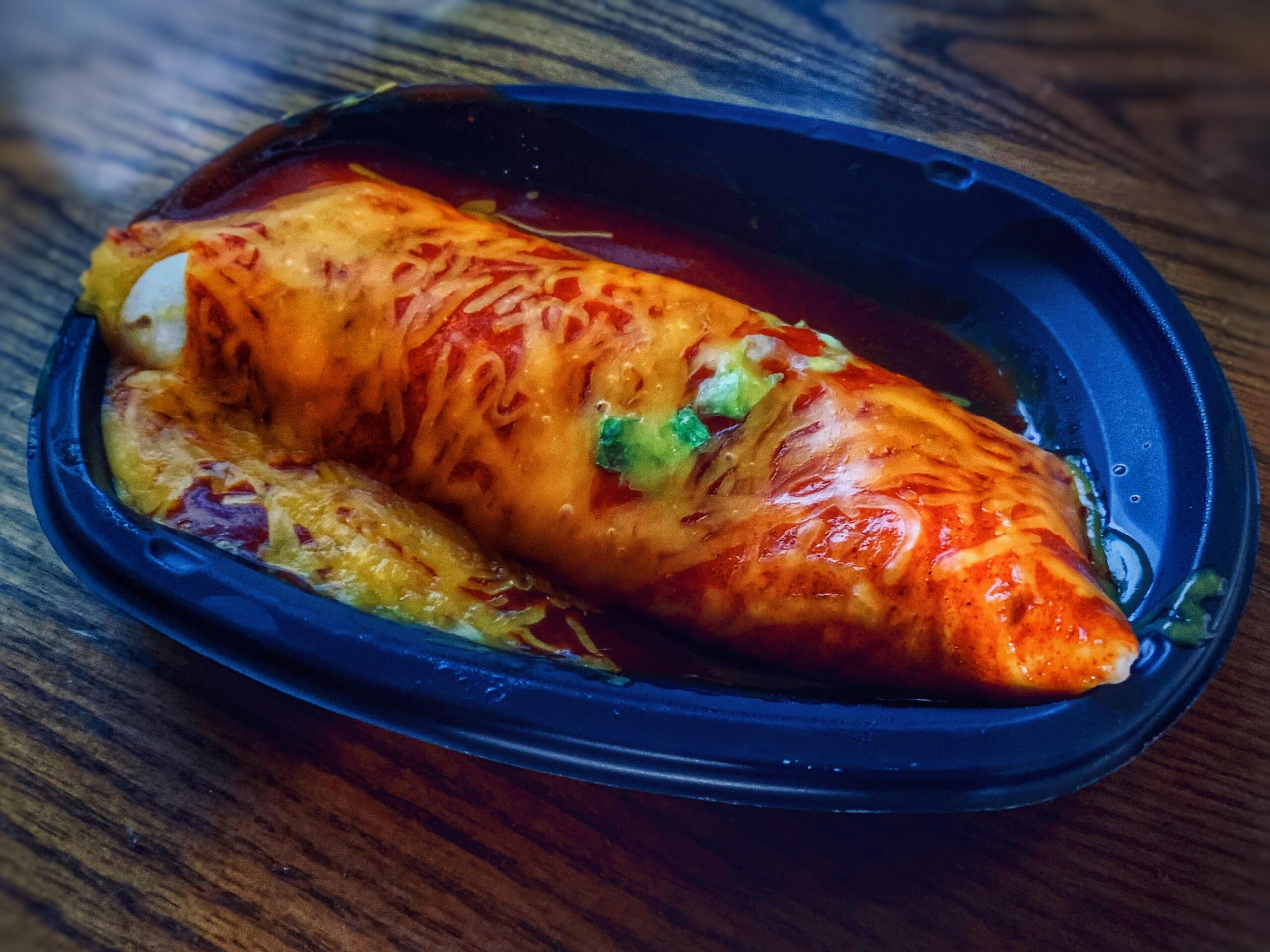 A smothered burrito topped with melted cheese and red sauce in a black plastic tray, one of the fast-food comebacks meal.