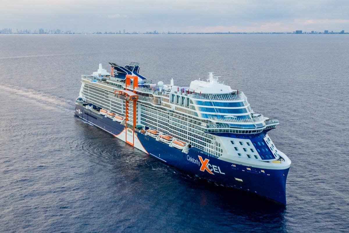 The Celebrity Xcel cruise ship sails on the open ocean toward a distant city skyline, offering guests views from its expansive cruise ship buffets.