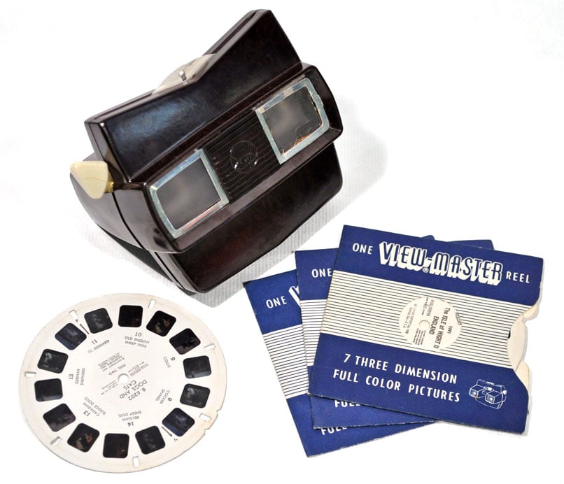 A vintage brown View-Master stereoscope with one circular image reel and several paper reel sleeves.