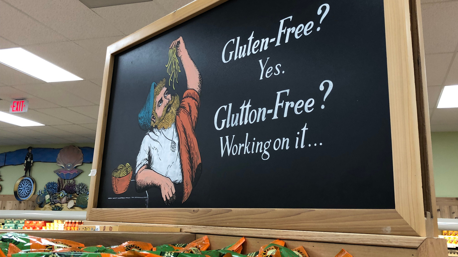 A chalkboard sign featuring an illustration of a bearded man eating pasta, with the text: “Gluten-Free? Yes. Glutton-Free? Working on it...”