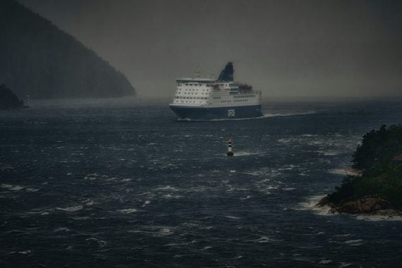 A large DFDS ferry travels through choppy, dark water on a stormy day.