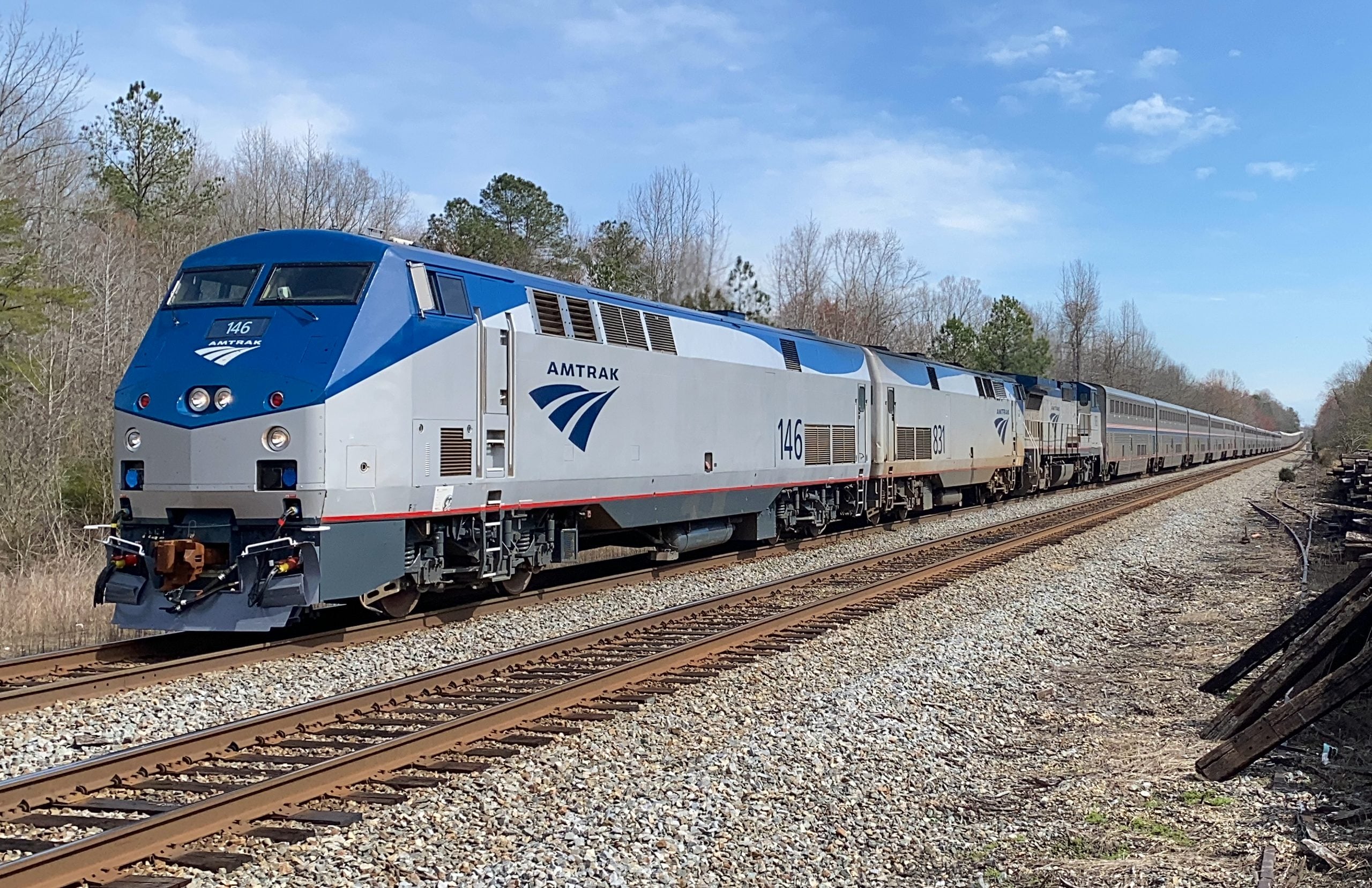 An Amtrak passenger train led by locomotive 146 travels along railway tracks through a wooded area.
