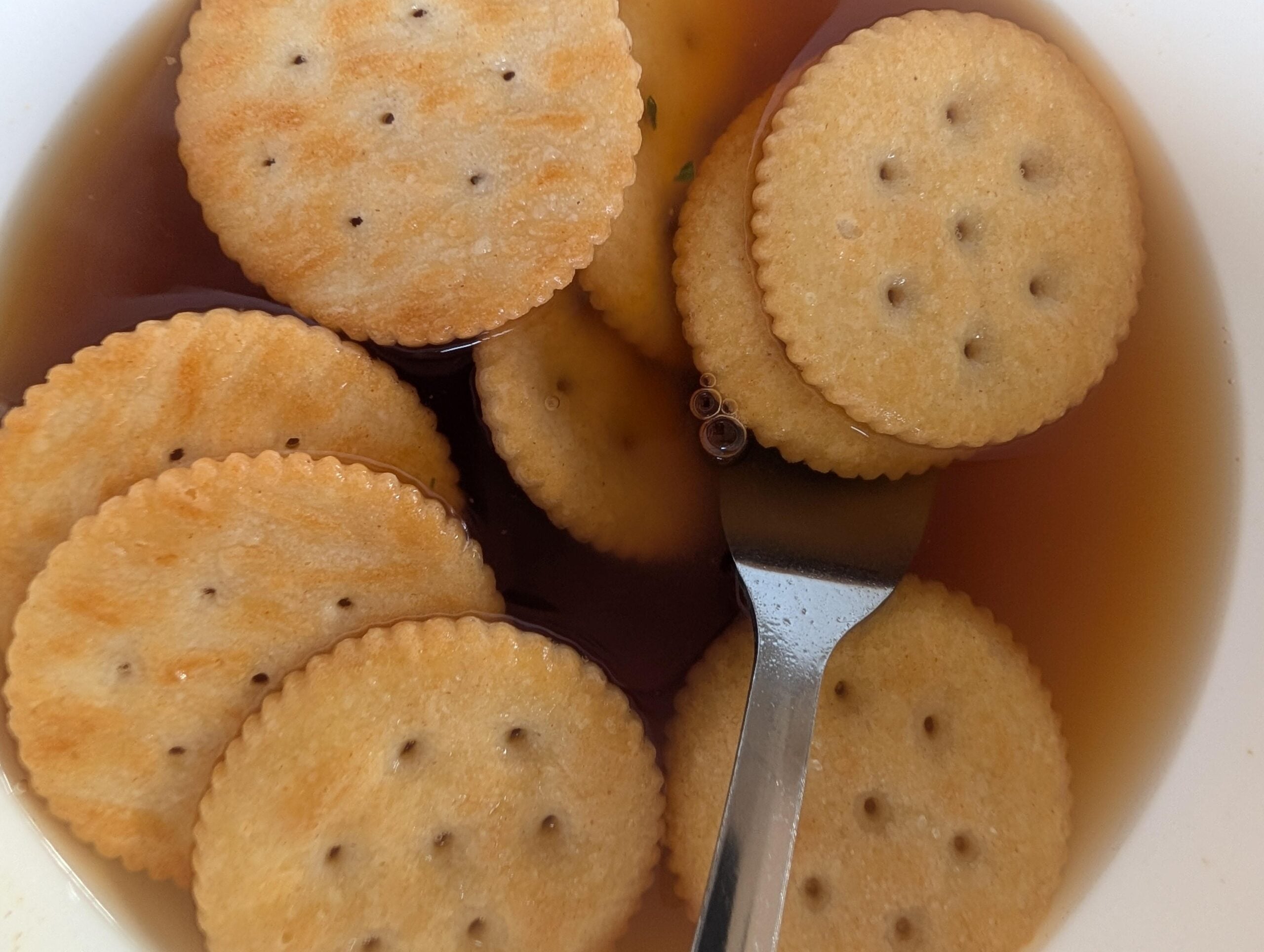 Round crackers floating in a bowl of brown broth with a metal spoon.