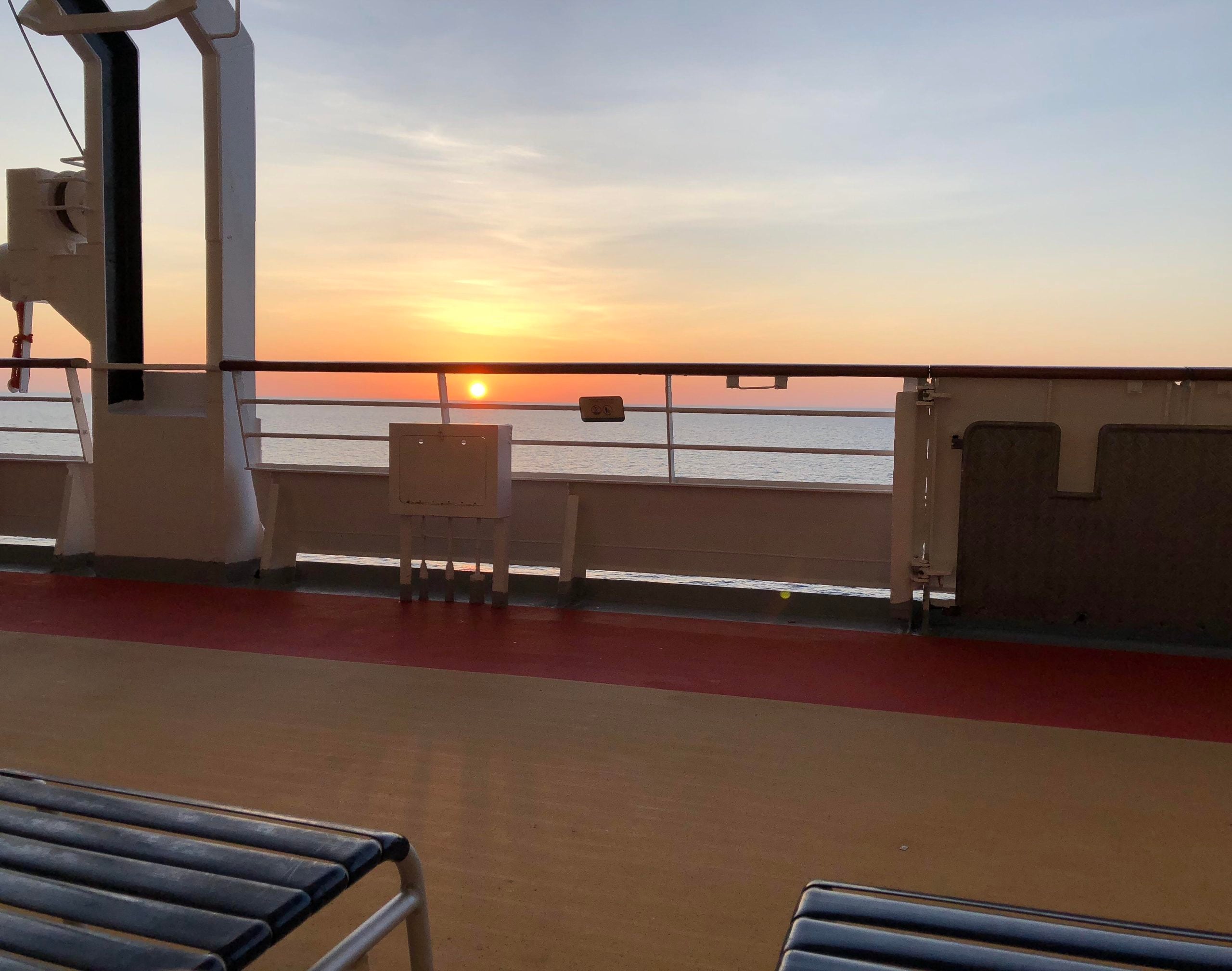 The sun setting over the ocean, viewed from the deck of a ship.