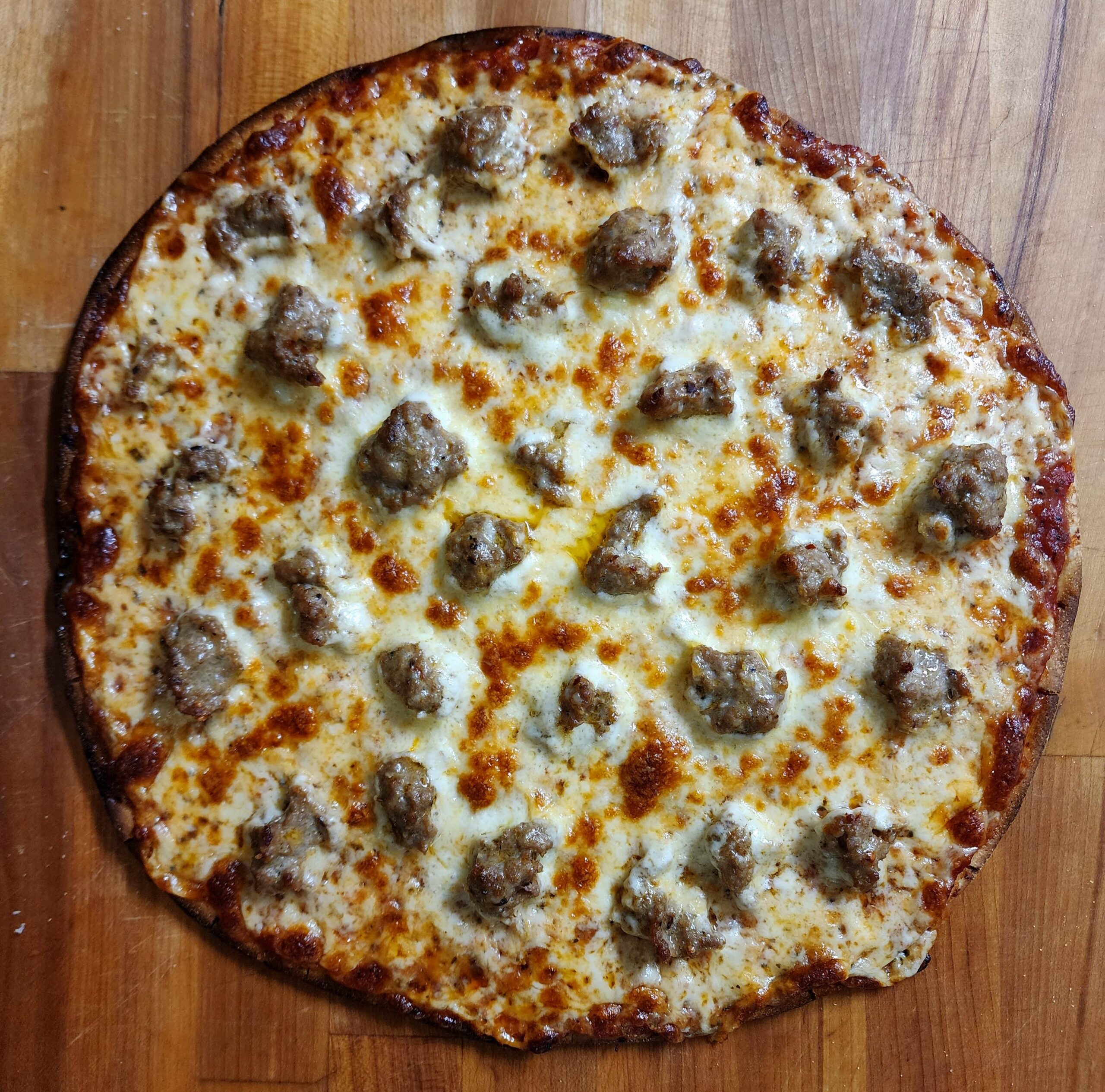A cooked sausage pizza with a golden-brown crust, melted cheese, and evenly distributed sausage pieces on a wooden surface.