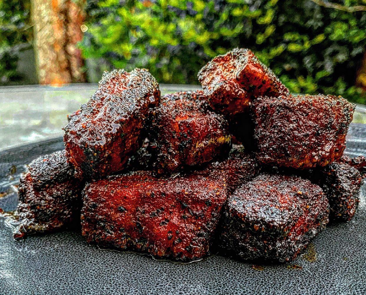 A pile of glazed, dark-crusted pork belly burnt ends on a textured gray plate.