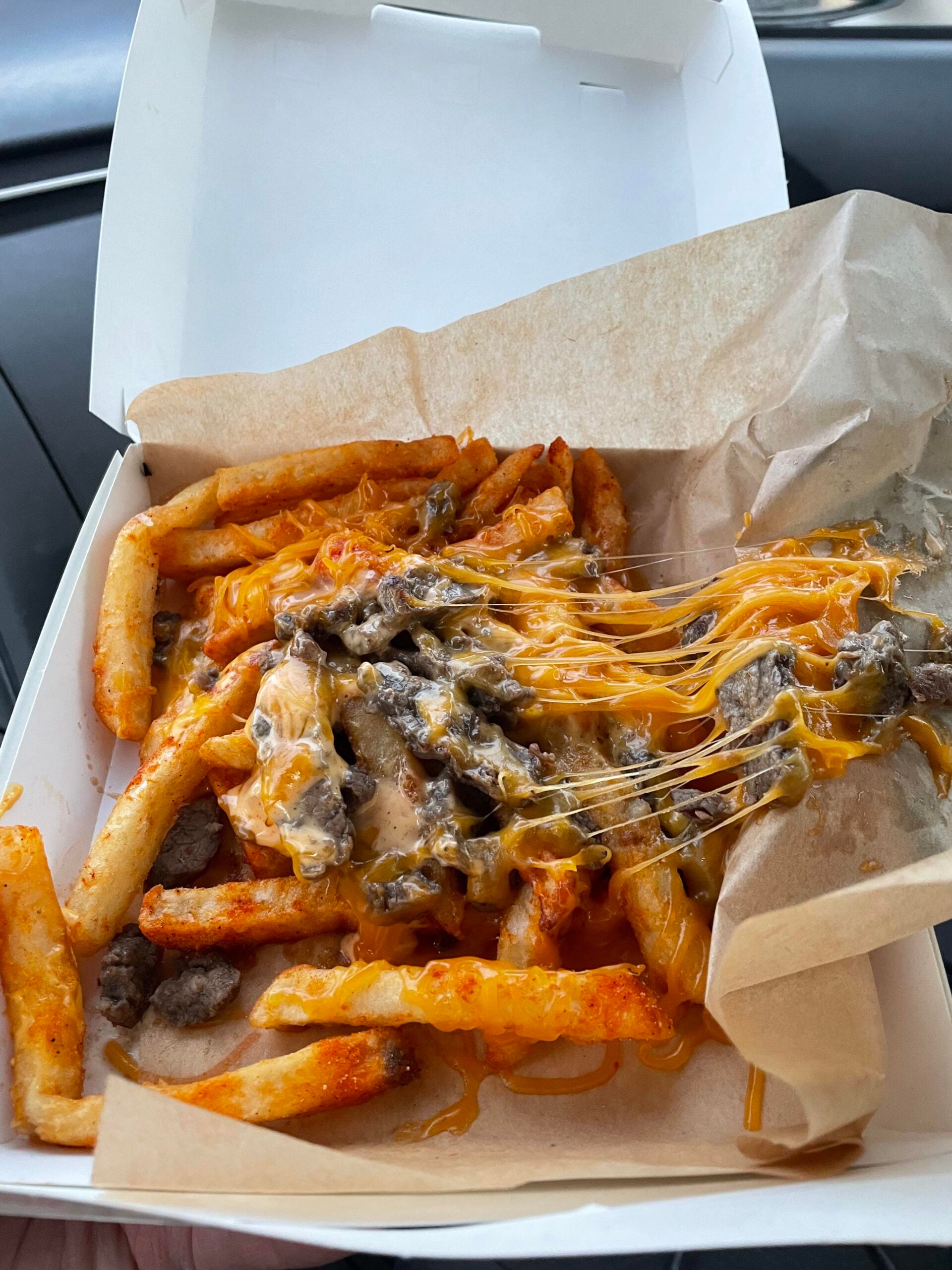 French fries topped with melted cheese and pieces of steak in a cardboard takeout box, one meal on the fast-food menus.