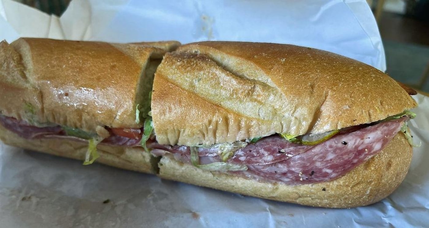 A sliced Italian sub sandwich on a baguette with salami, lettuce, and tomatoes.